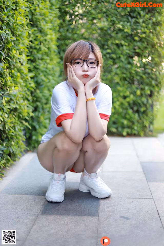 A woman wearing glasses crouching down on a sidewalk.