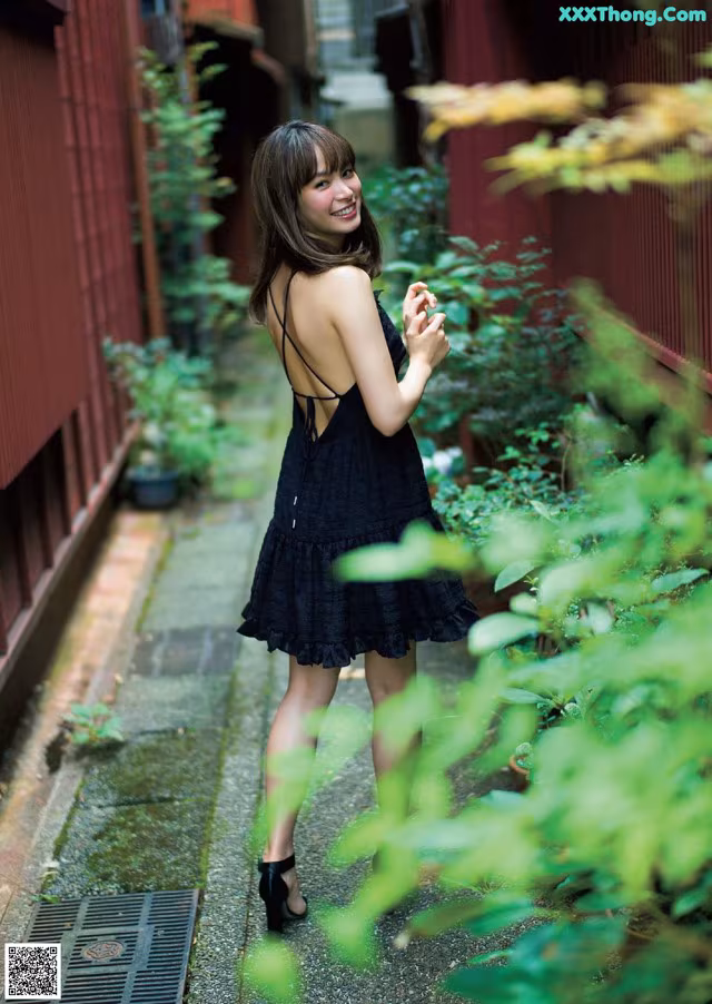 A woman in a black dress standing on a sidewalk.