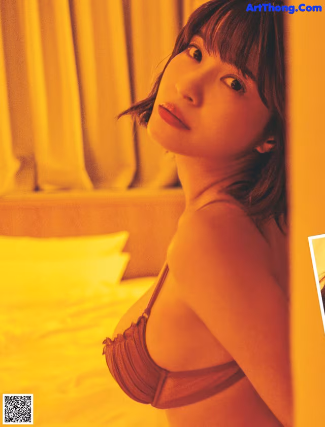 A woman in a brown bikini standing in front of a bed.