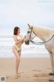 A woman in a white bikini standing next to a white horse.