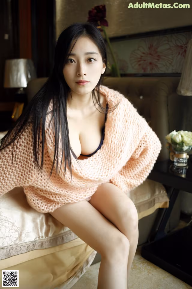 A woman sitting on top of a bed in a pink sweater.