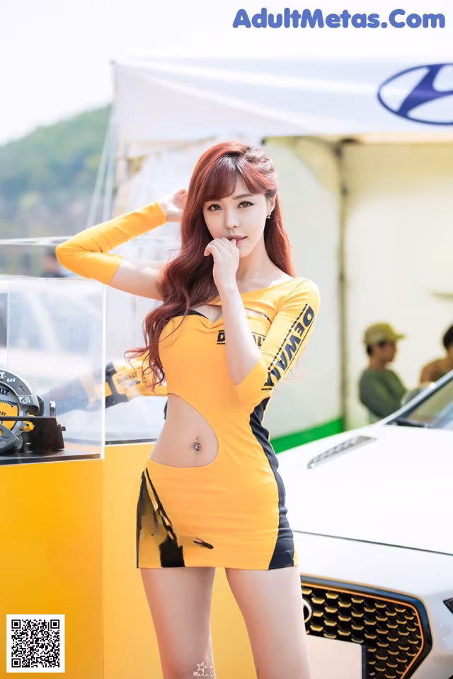 A woman in a yellow and black dress standing next to a car.