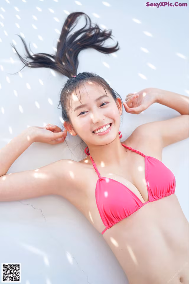 A woman in a pink bikini laying on a white surface.