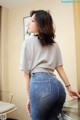 A woman in a gray shirt and blue jeans leaning against a glass table.