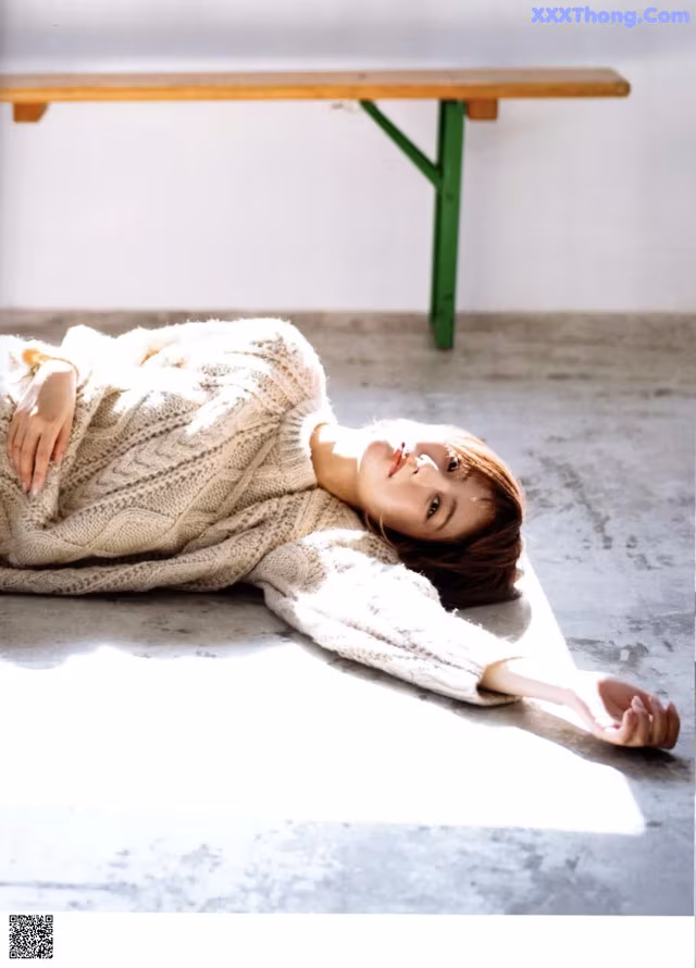 A woman laying on the floor in a white sweater.