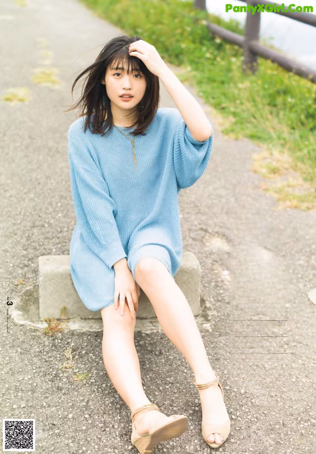 A woman sitting on a concrete bench wearing a blue sweater dress.