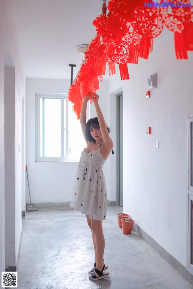 A woman in a white dress holding up a red chandelier.