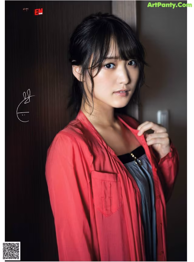 A woman in a red shirt leaning against a wall.