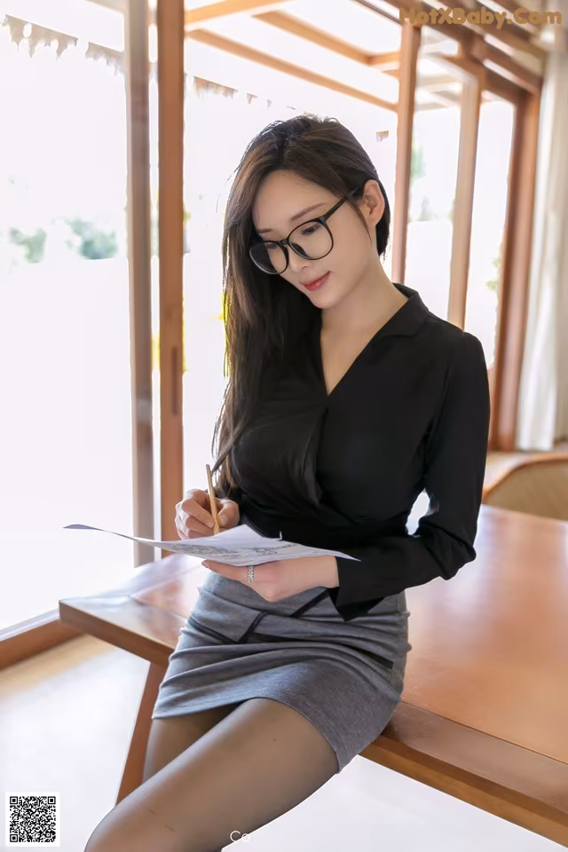A woman sitting at a table writing on a piece of paper.