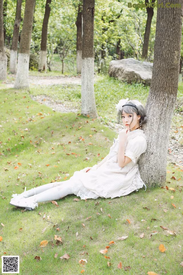 A woman in a white dress sitting under a tree.