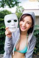 A woman in a bikini holding up a white mask.